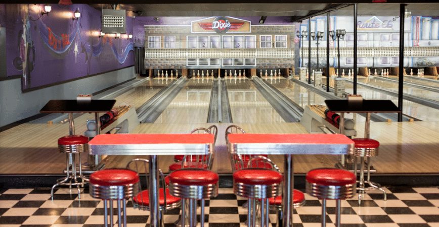 Inside Alder Alley: red diner stools and checkerboard floor in front of the five-pin lanes, with retro signs above the pins