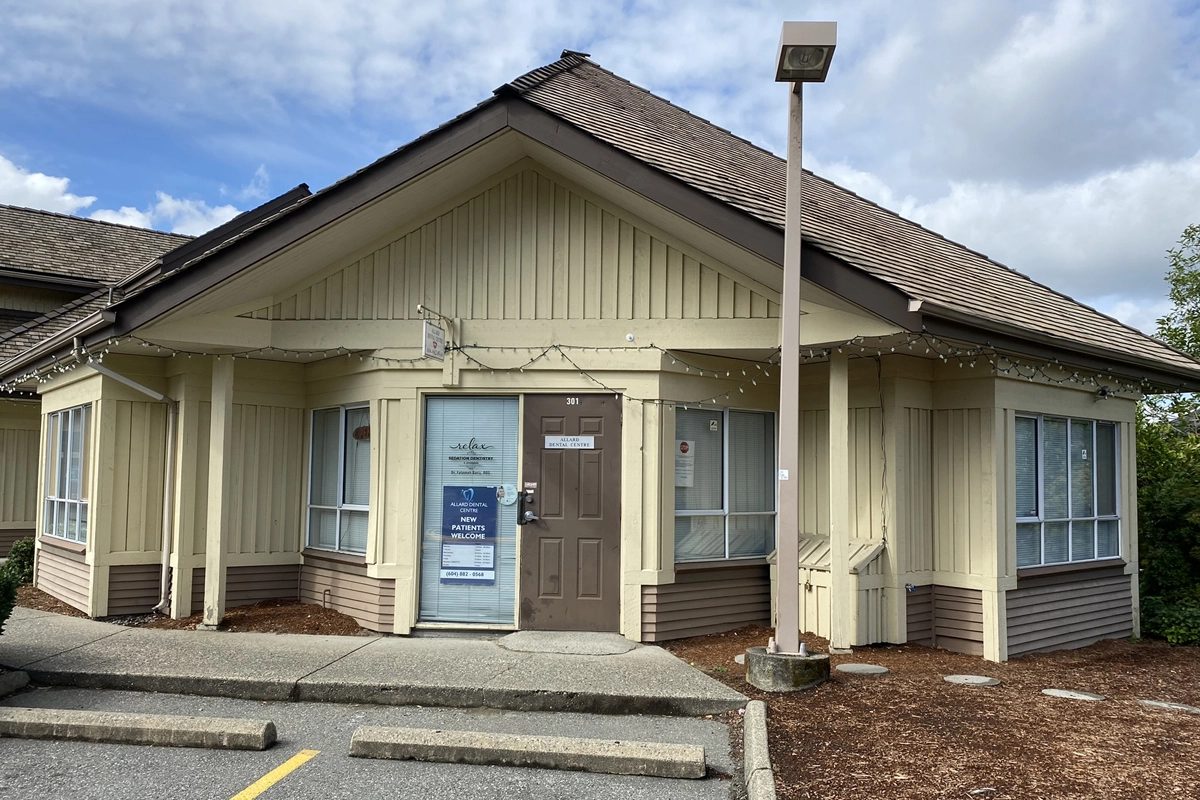 The front of Allard Dental Centre, unit 301: a one-storey cream building with a brown door and a New Patients Welcome sign in the glass beside it, with parking out front