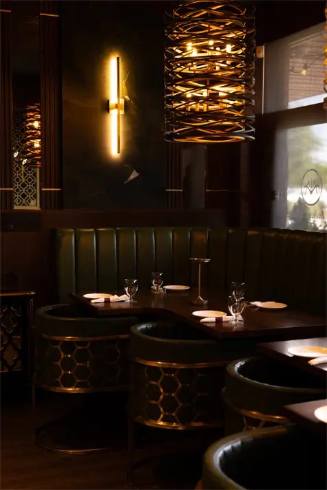 The dining room at An Indian Affair: green upholstered booths, dark wood tables and a glowing woven pendant light