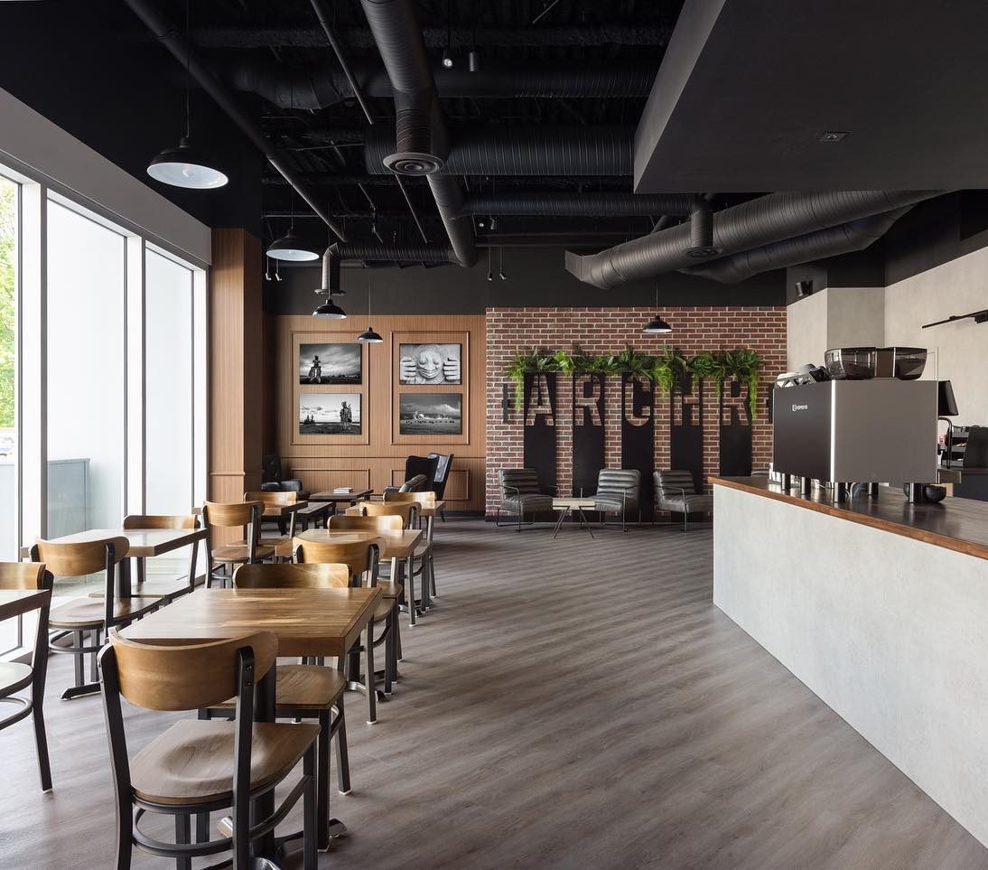 Inside ARCHR: wooden tables and chairs on a grey floor, big windows, black ductwork and an ARCHR sign on the brick feature wall