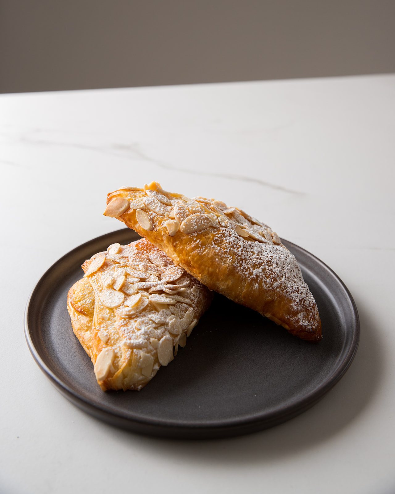 Two almond croissants dusted with icing sugar on a dark plate