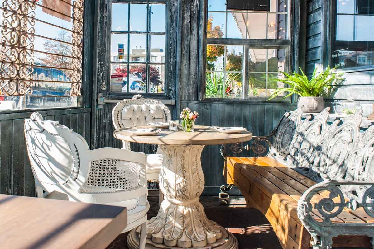 The enclosed sunroom at Ban Chok Dee: a round white pedestal table, upholstered chairs and a cast-iron bench beside tall windows