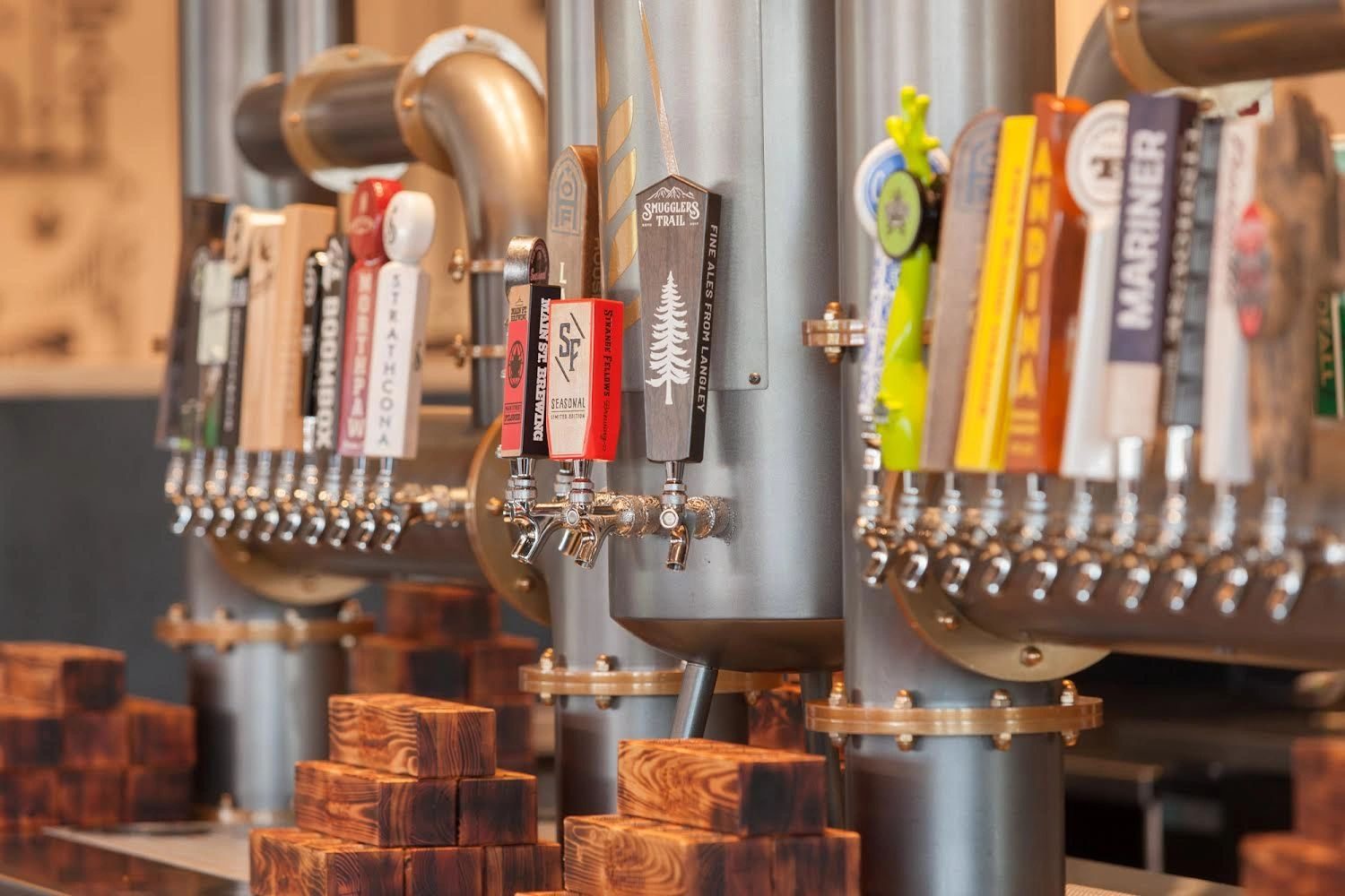 The long tap wall at The Barley Merchant, with BC brewery tap handles and copper pipes