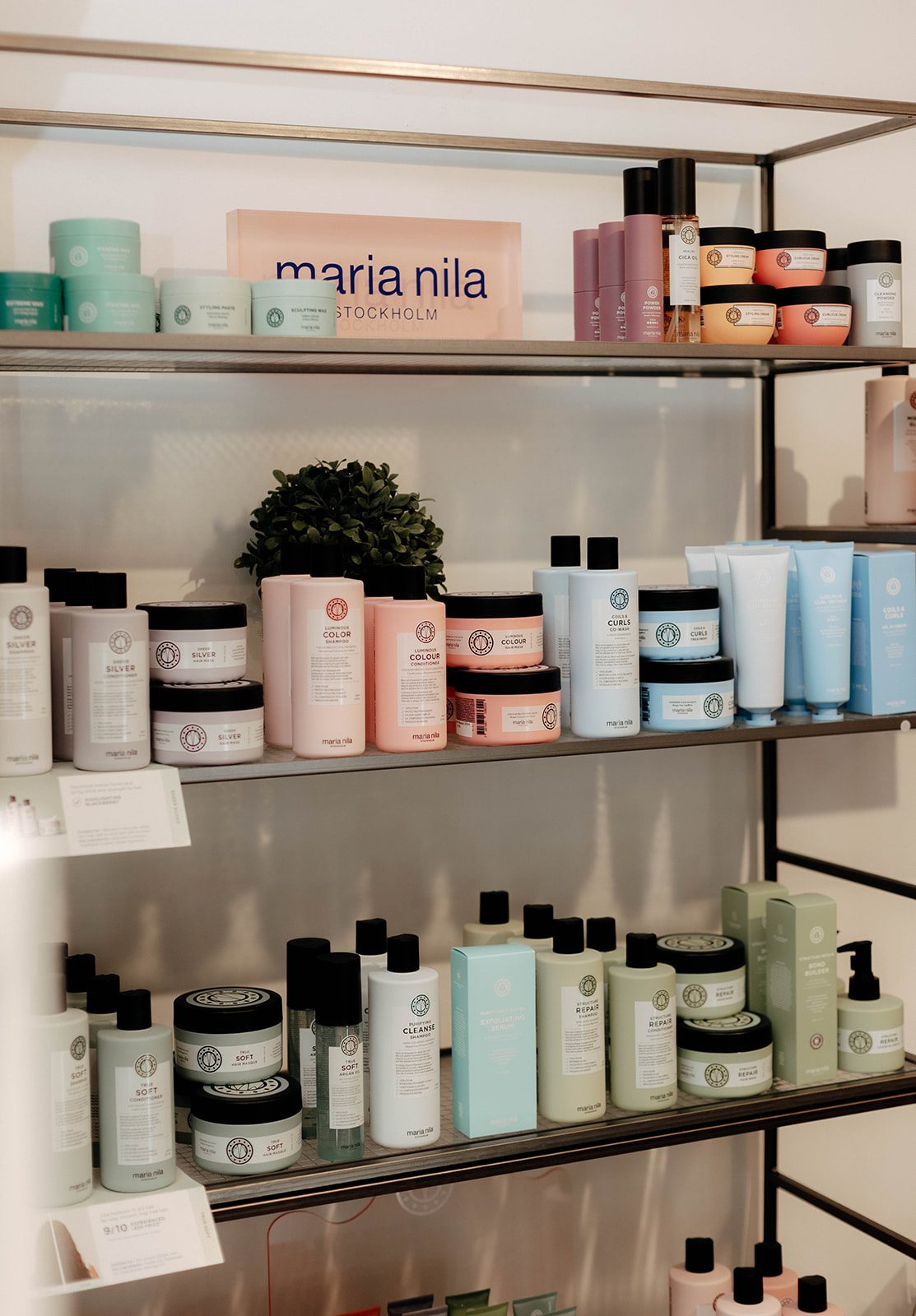 Shelves of Maria Nila haircare in pastel bottles and jars, with a pink acrylic Maria Nila Stockholm sign on the top shelf