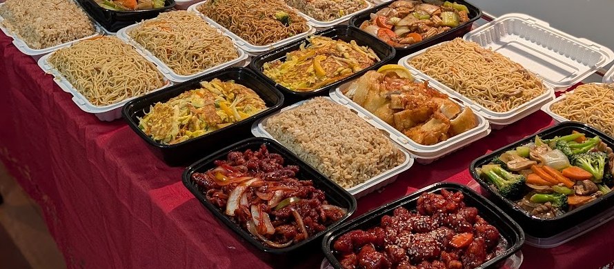 A red tablecloth covered in China Bowl take-out containers: chow mein, fried rice, egg foo young, lemon chicken, ginger beef, sesame-topped chicken and mixed vegetables