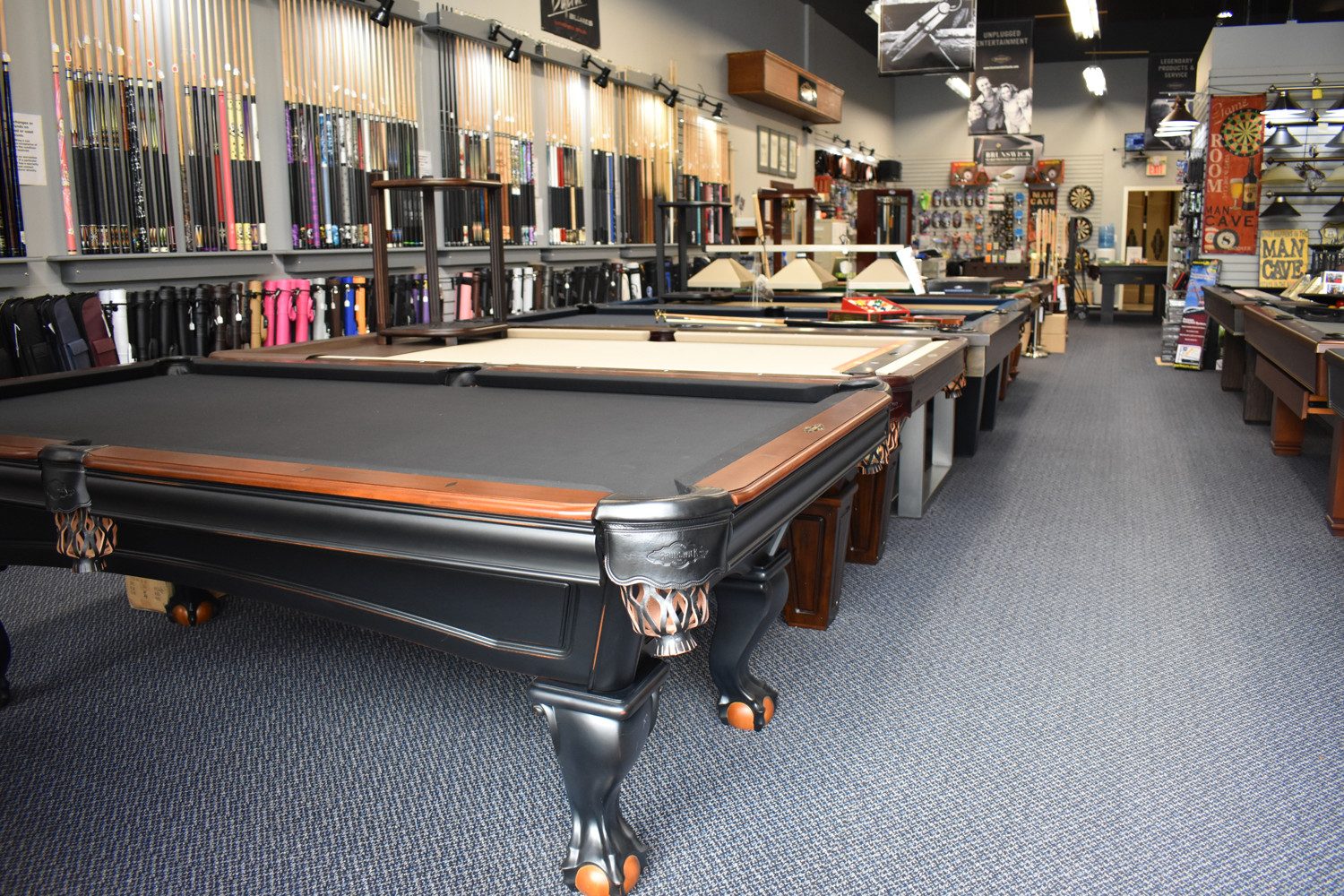 Pool tables lined up on the showroom floor at Classic Games and Billiards, with racks of cues along the walls