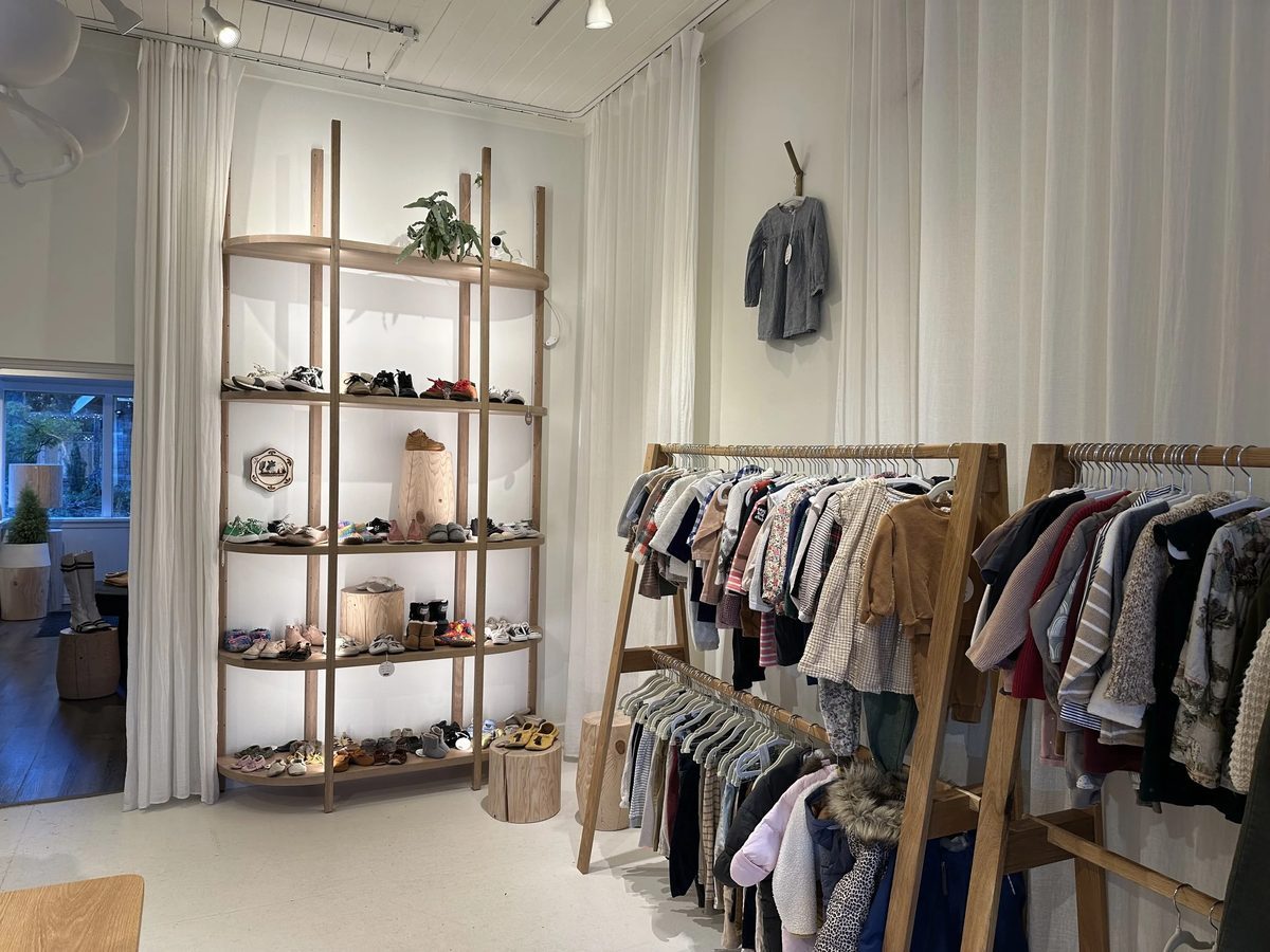 Inside Cowboy Circus Kids Market: low wooden rails of children's clothes and open shelves of little shoes in a bright white shop