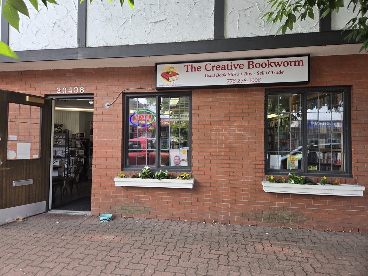 The Creative Bookworm's red-brick storefront on Douglas Crescent in downtown Langley, with flower boxes under the windows and the door propped open