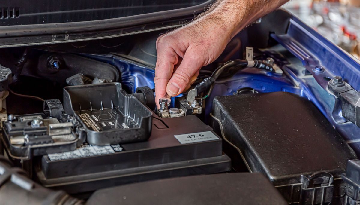 A technician's hand fitting a new battery under the hood of a car