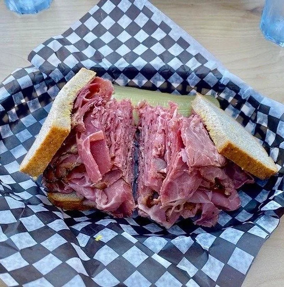 A smoked meat sandwich piled high on rye in a checkered paper-lined basket