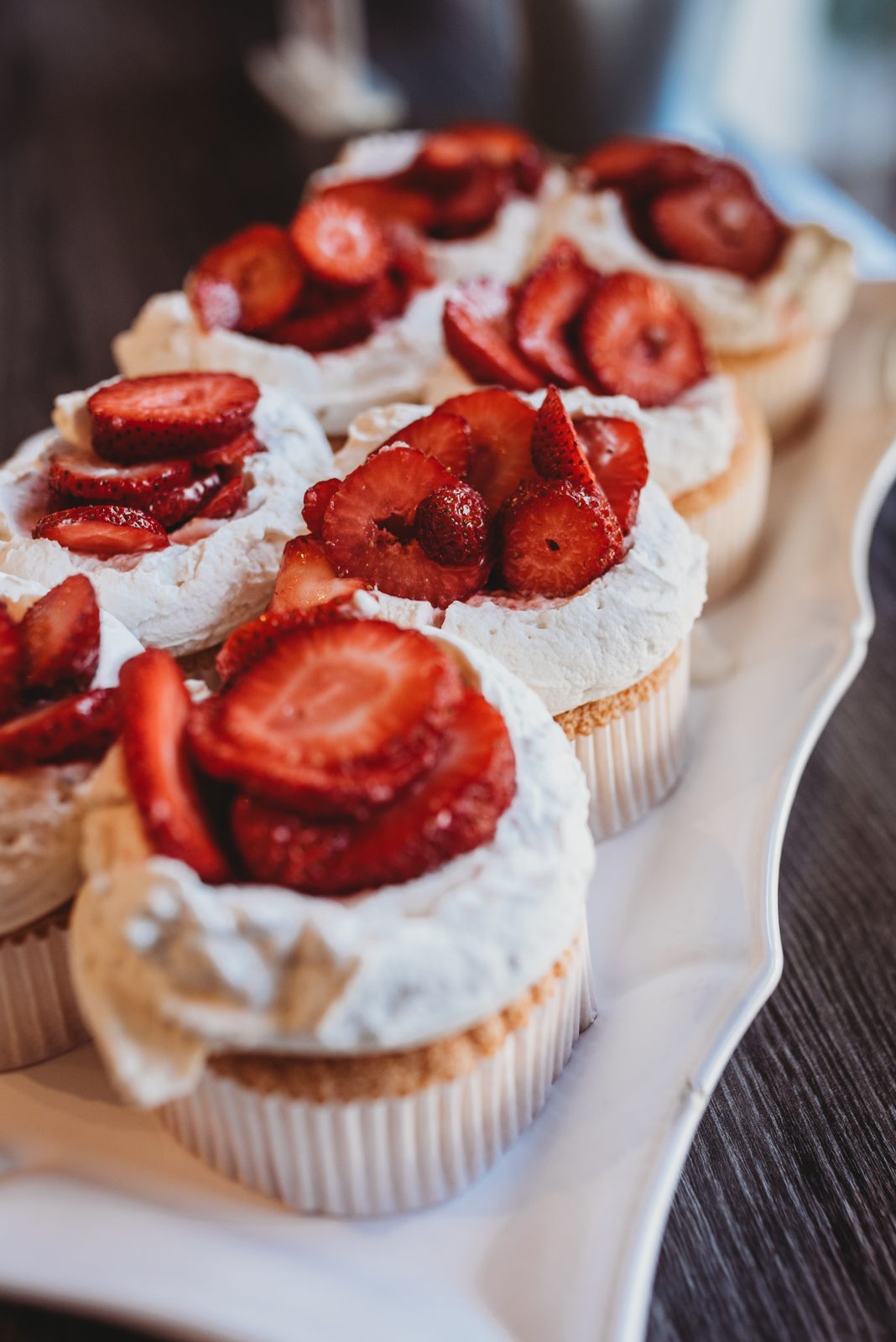 Cupcakes topped with whipped cream and sliced strawberries on a white platter