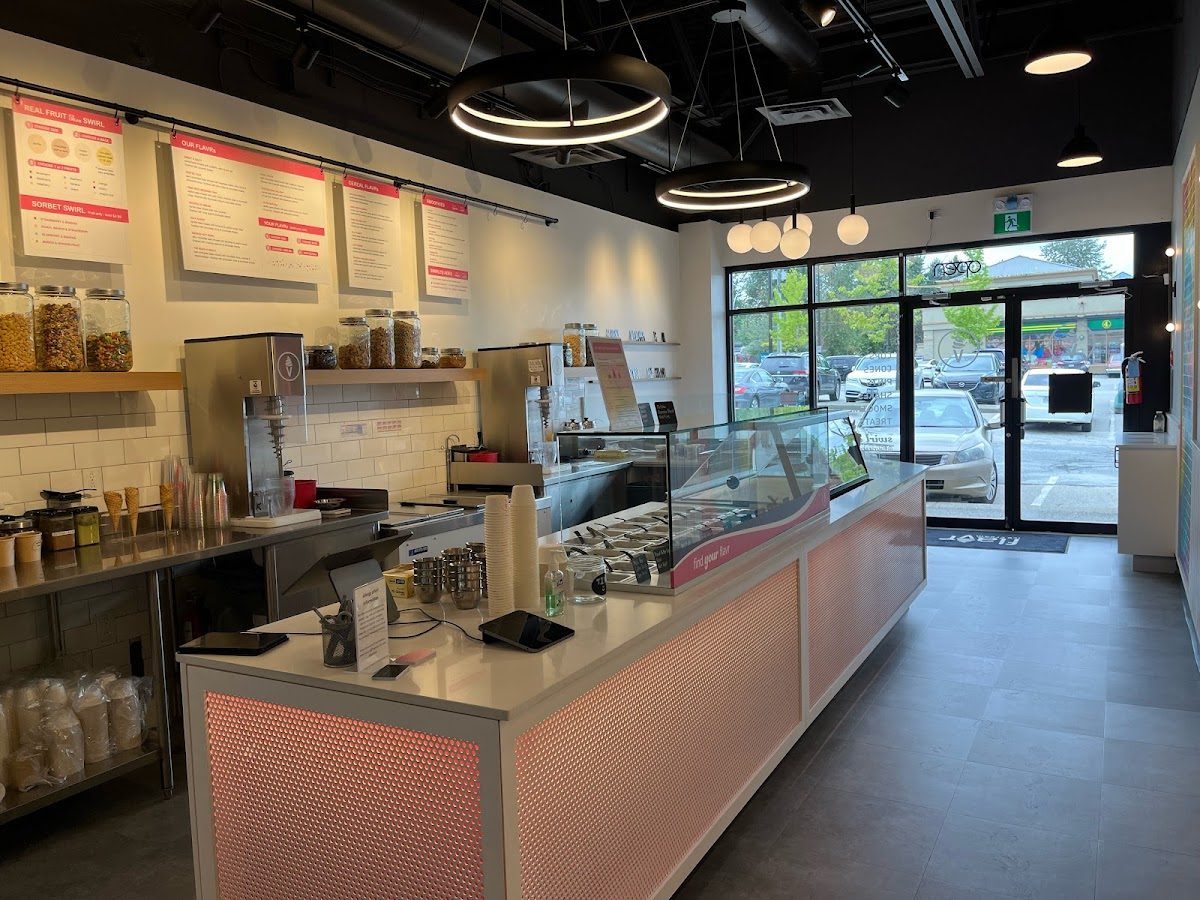 Inside Flavr Ice Cream: a long white counter with a glass display case, menu boards overhead and ring pendant lights