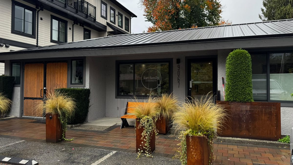 The Fort Family Chiropractic front on Church Street: grey stucco, a round logo in the window, rusted-steel planters with feather grass and a wooden bench, autumn trees behind