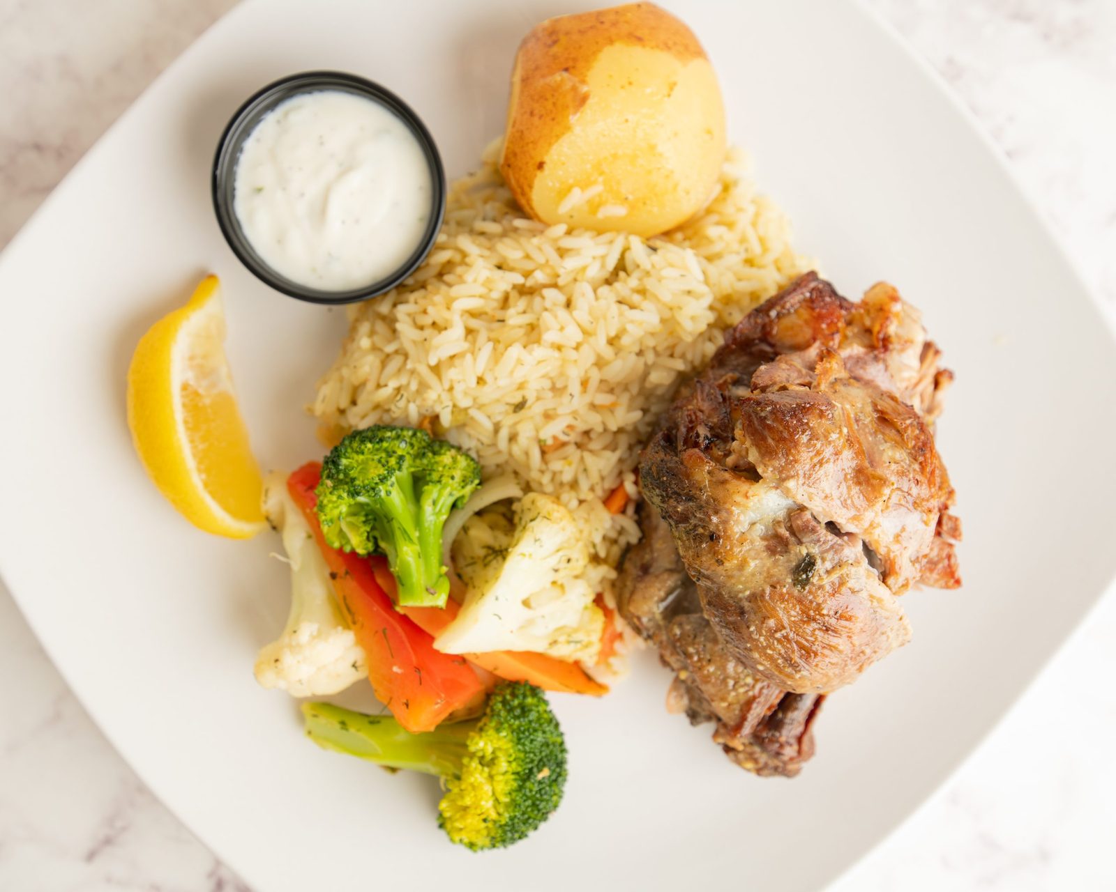 A plate of Galini's roast lamb with rice, roast potato, vegetables, lemon and tzatziki