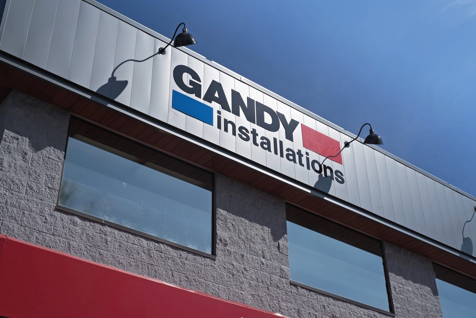 The Gandy Installations sign in blue, red and black lettering on the silver-panelled front of the company's head office in Langley, against a blue sky