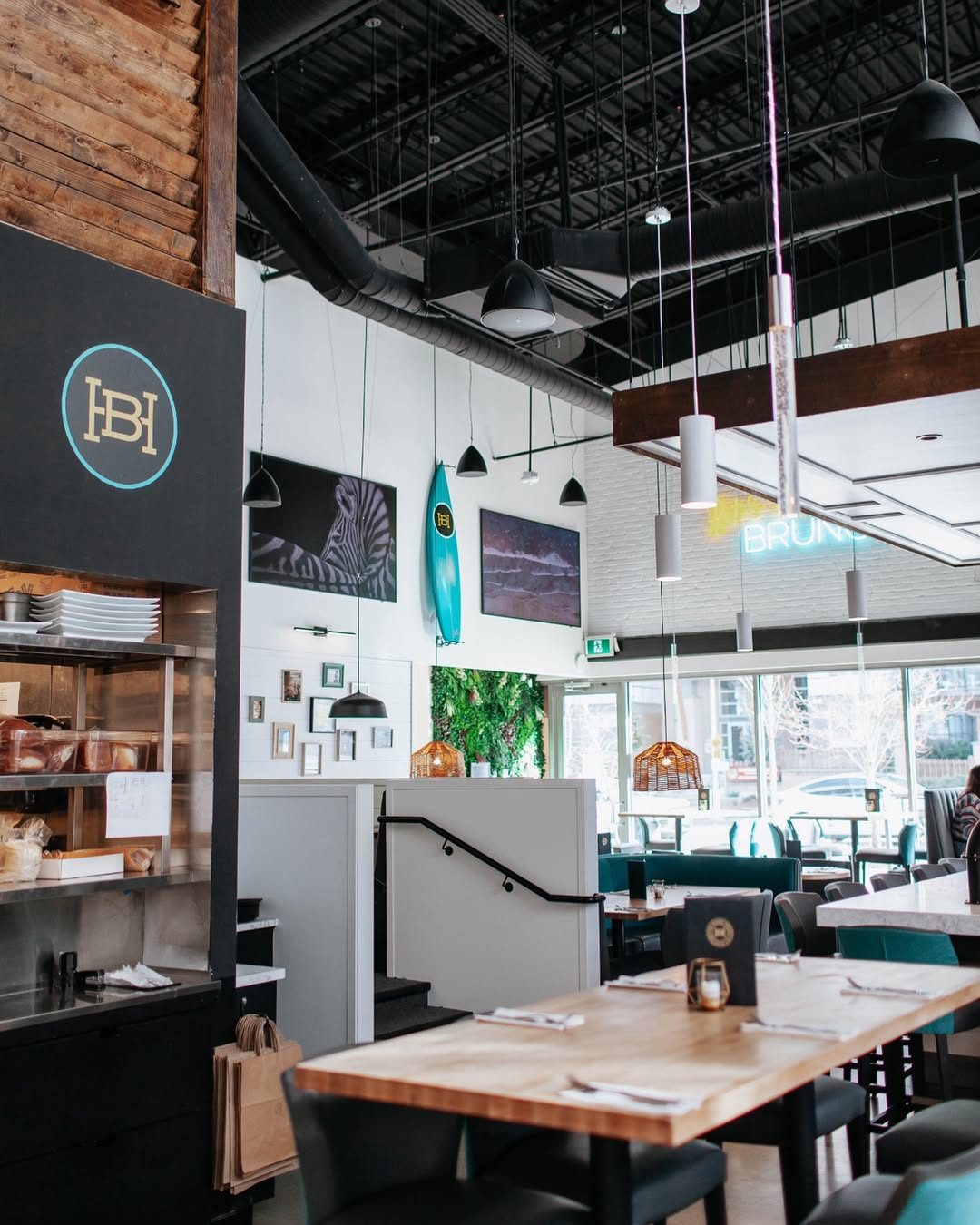 The Hard Bean's Willoughby dining room: high black ceiling with pendant lights, wooden tables, teal seating and a raised dining area