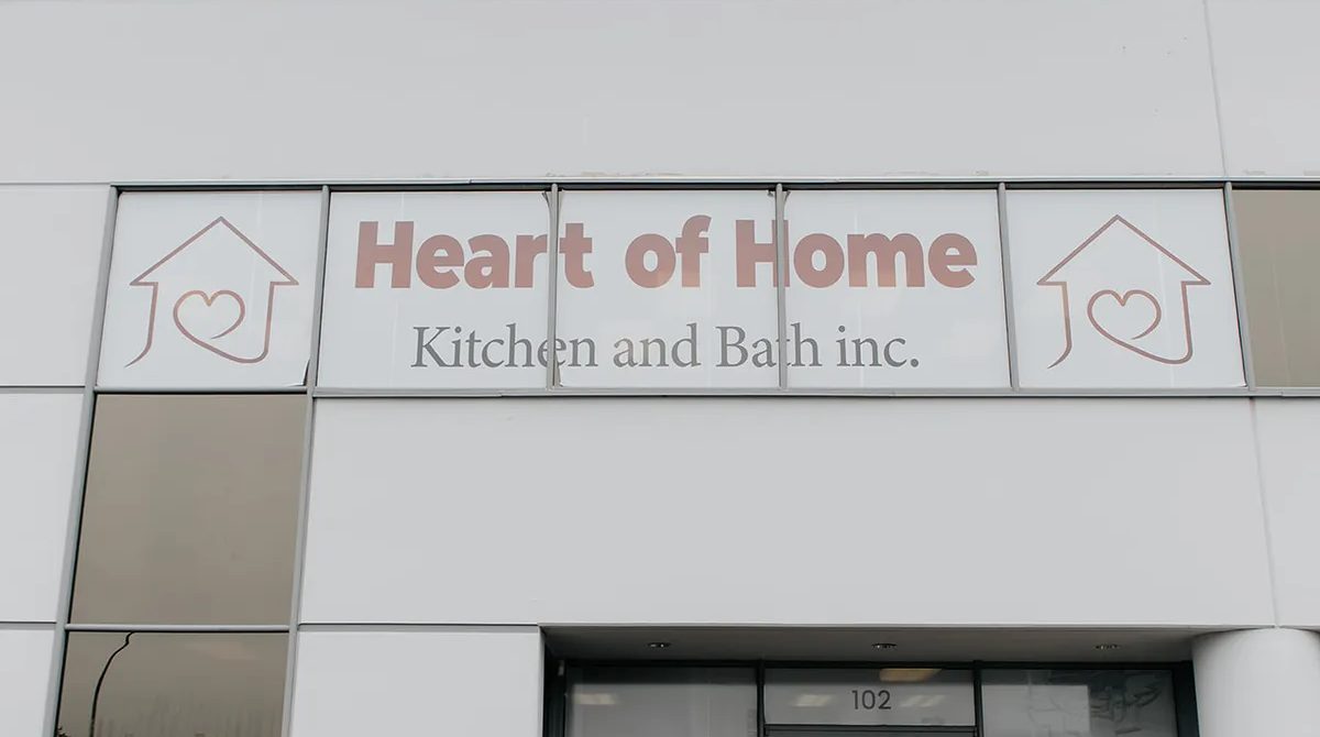 The Heart of Home Kitchen and Bath inc. sign with two house-and-heart logos on the grey front of the building, with the door to unit 102 at the bottom edge