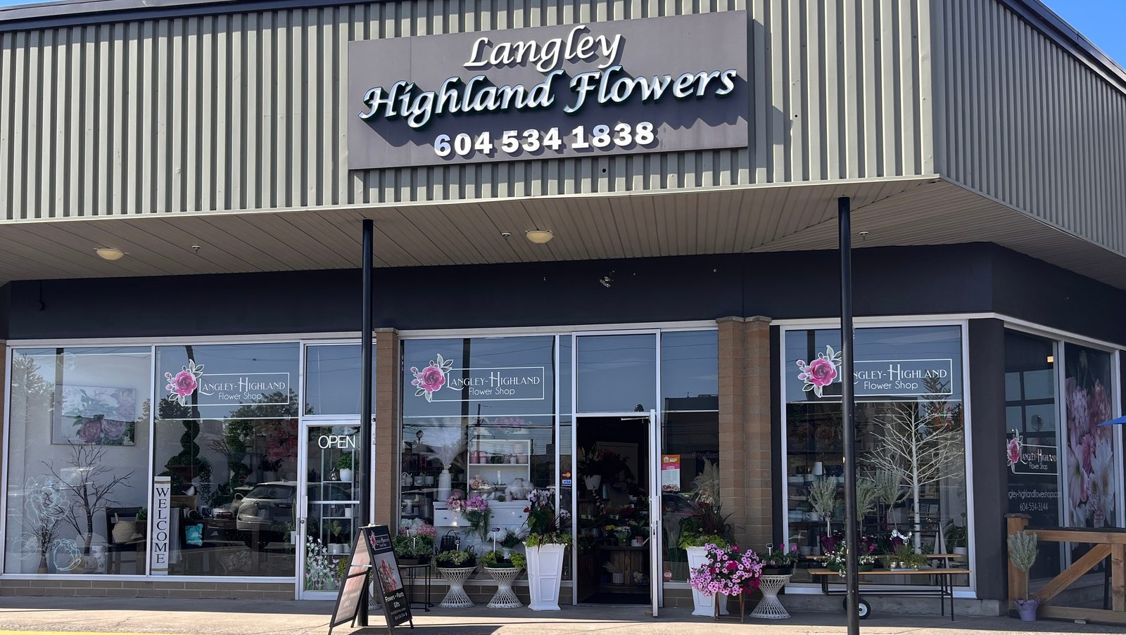The Langley Highland Flowers storefront, big windows with potted flowers and a sandwich board outside