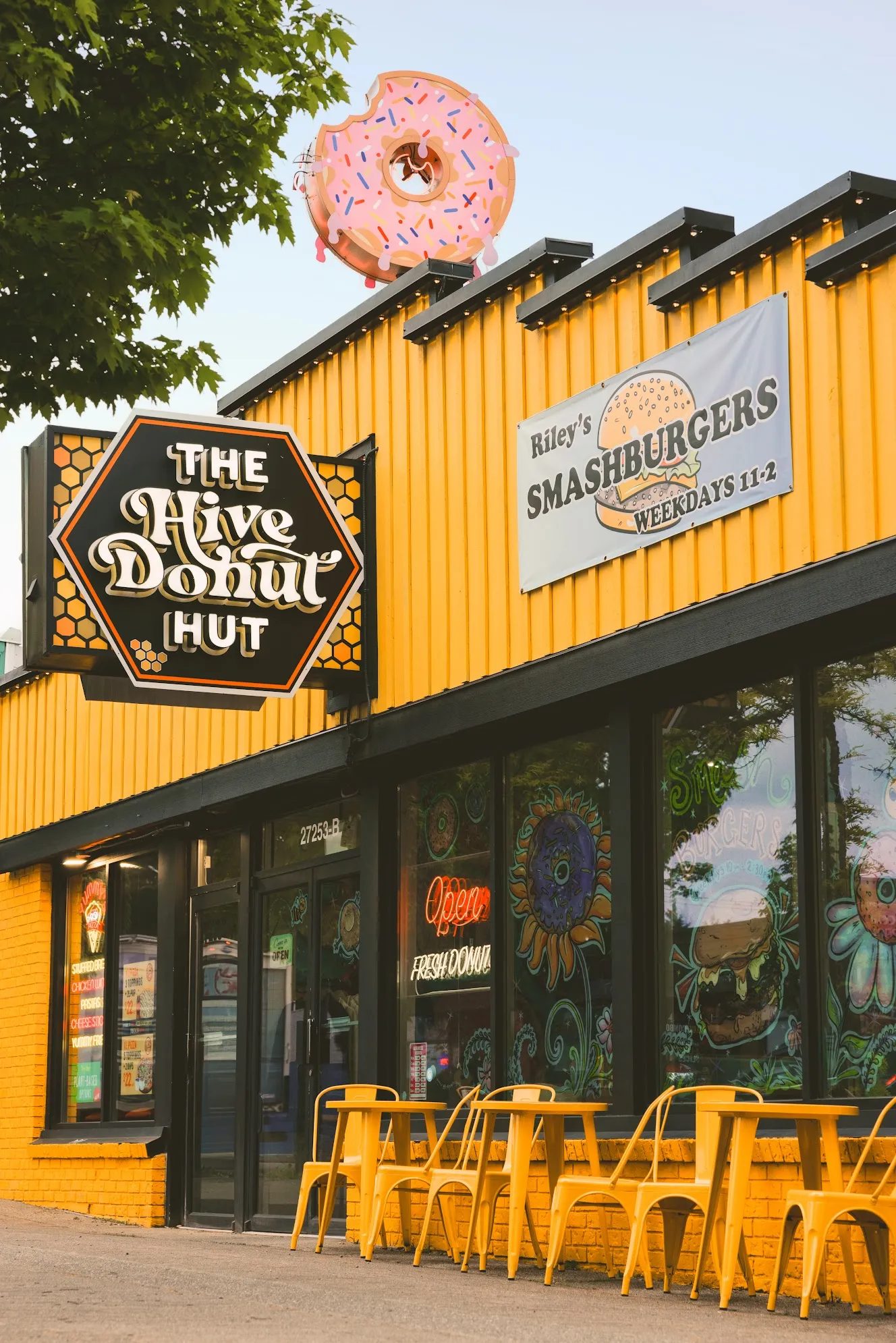 The Hive Donut Hut's bright yellow storefront on Fraser Highway, with yellow patio chairs out front and a giant pink donut on the roof