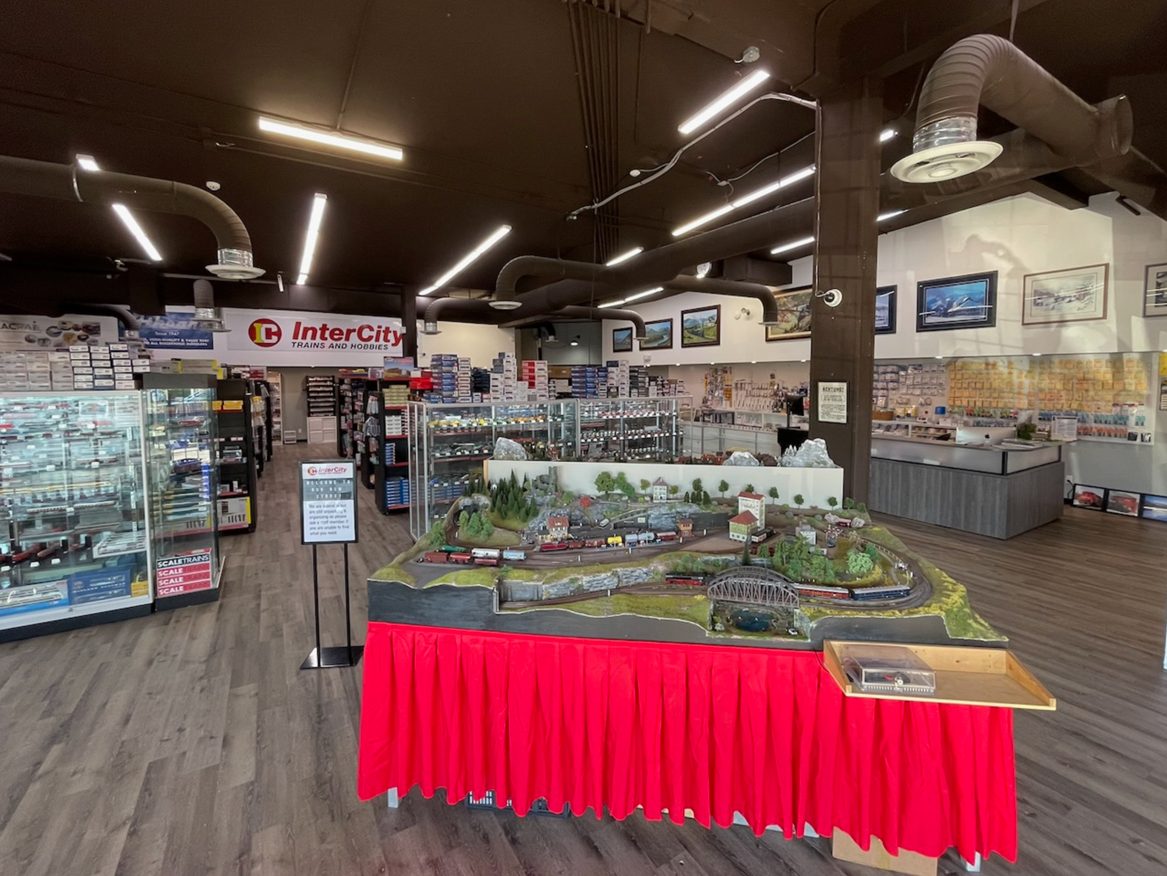 Inside InterCity Trains and Hobbies: a model railway layout on a red-skirted table in the middle of the showroom, with display cases and the InterCity sign behind