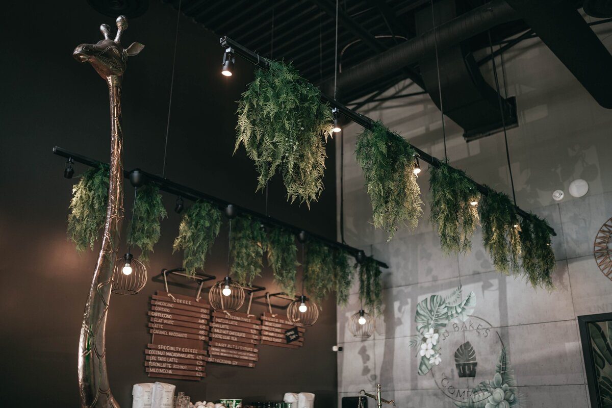Inside the JJ Bakes café: a tall giraffe sculpture, hanging ferns and wooden menu boards on a dark wall