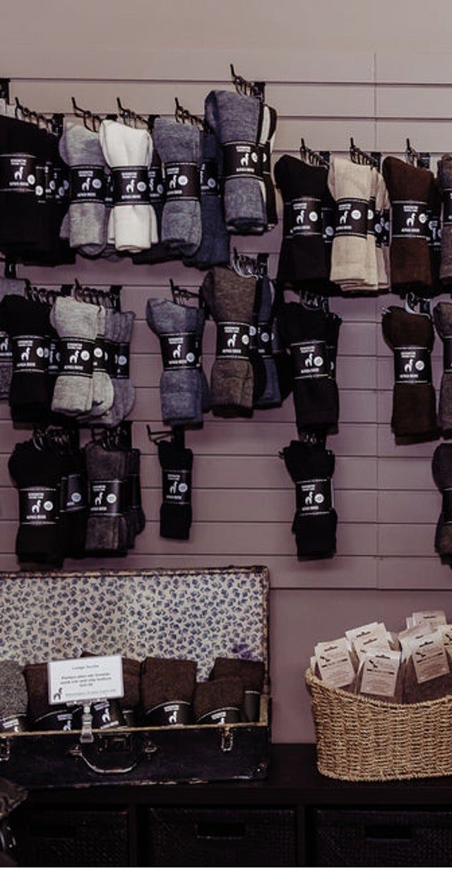 A slatwall of packaged alpaca socks in greys, browns and black inside the Kensington Prairie Farm boutique, with a vintage suitcase and a basket of socks below