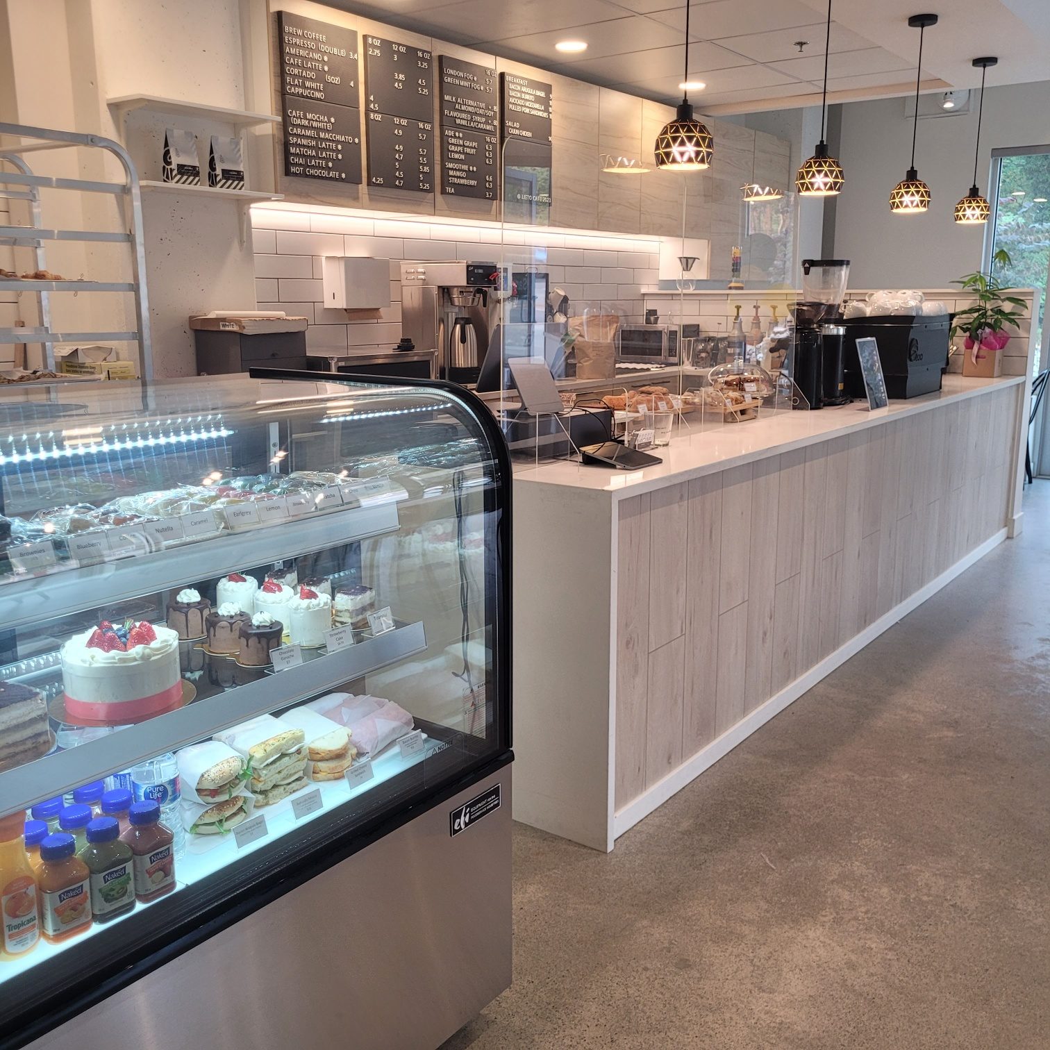 Inside Lieto Cafe: a glass case of cakes and sandwiches, a long white coffee counter, chalkboard menus and pendant lights