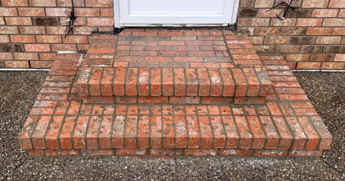 Rebuilt red-orange brick entry steps in front of a white door, with brick walls on either side