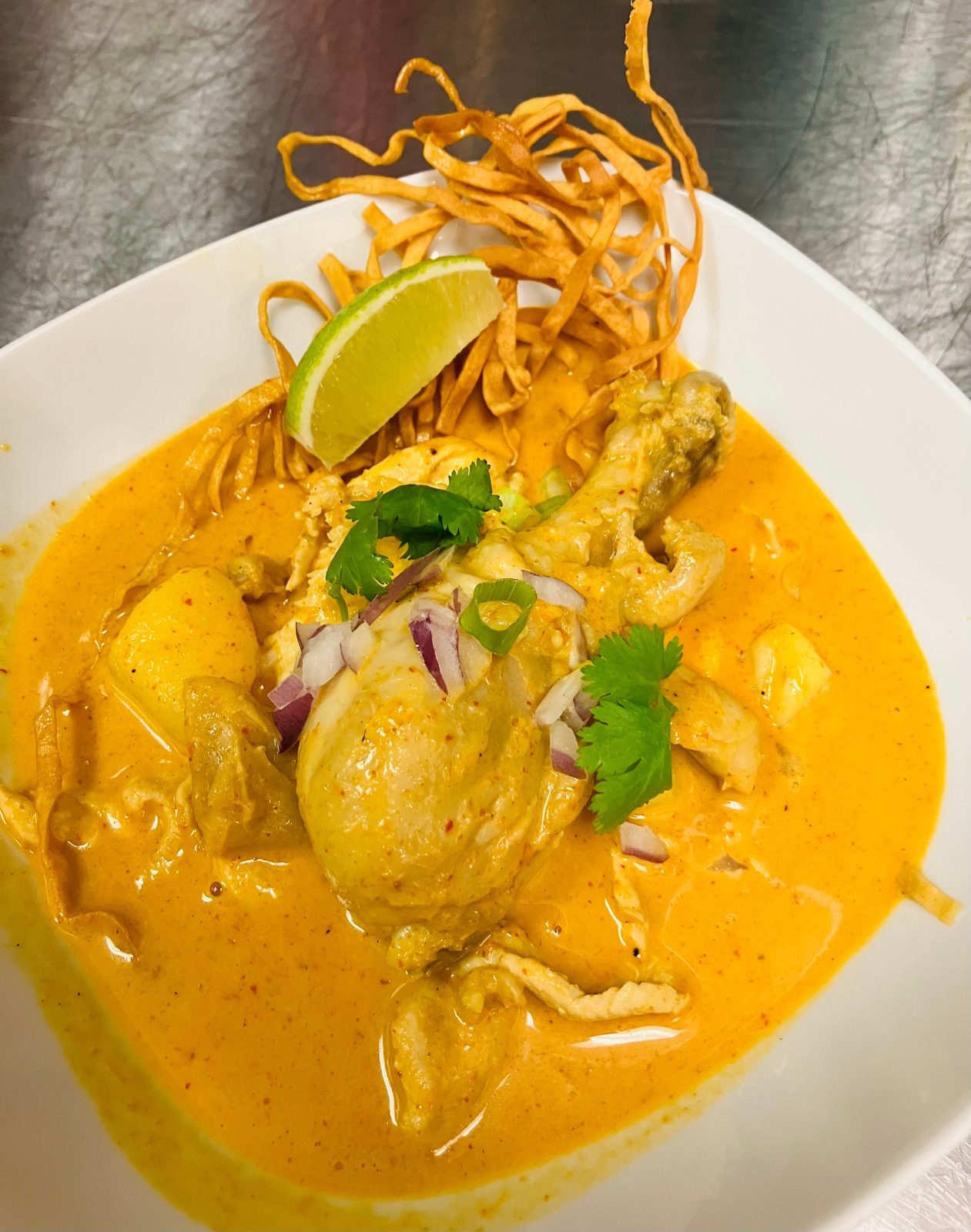 A bowl of Maple Thai's khao soi: chicken in yellow curry broth with crispy noodles, red onion, cilantro and a wedge of lime