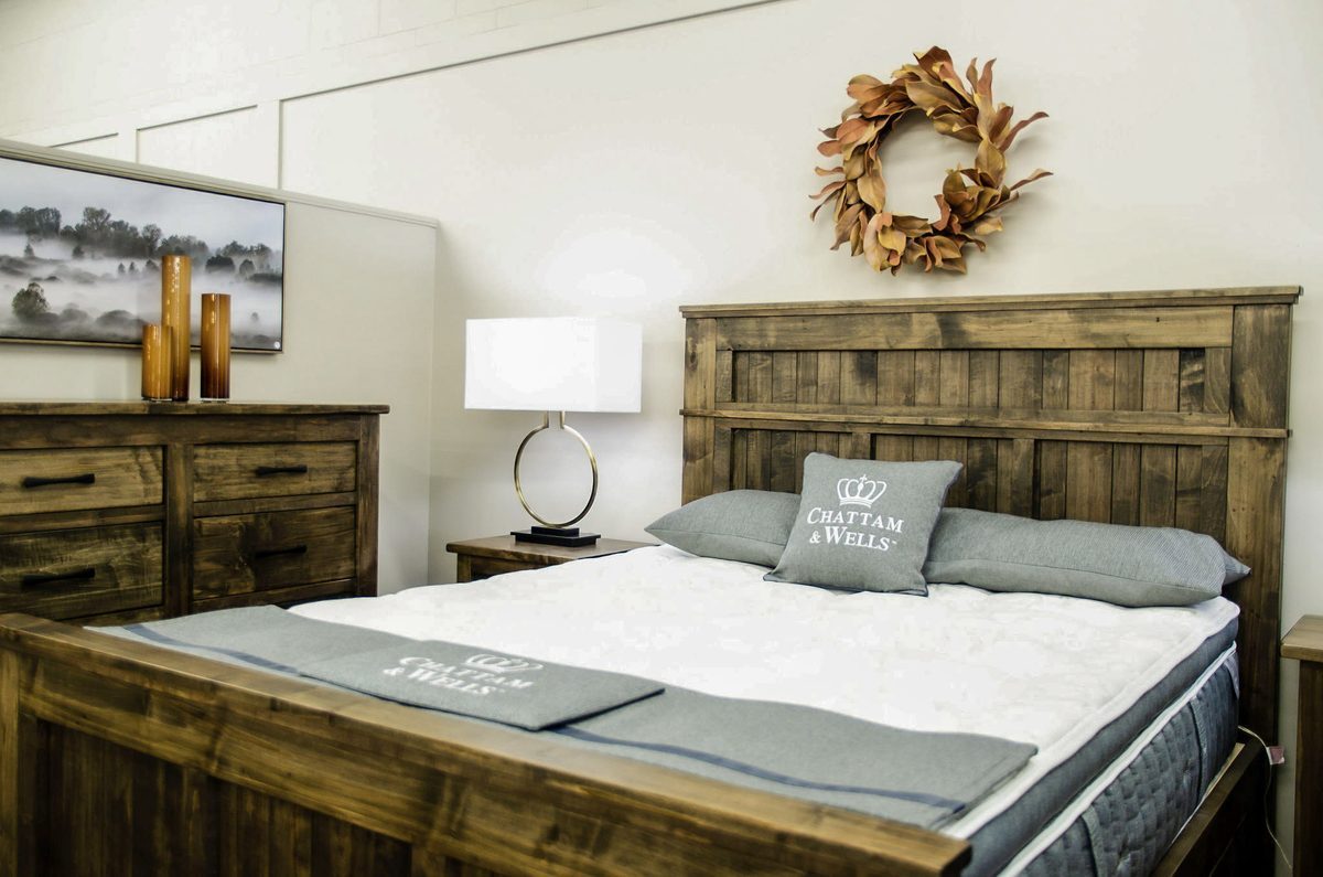 A McLeary's showroom bedroom: a rustic solid-wood bed and dresser with grey bedding and a wreath on the wall