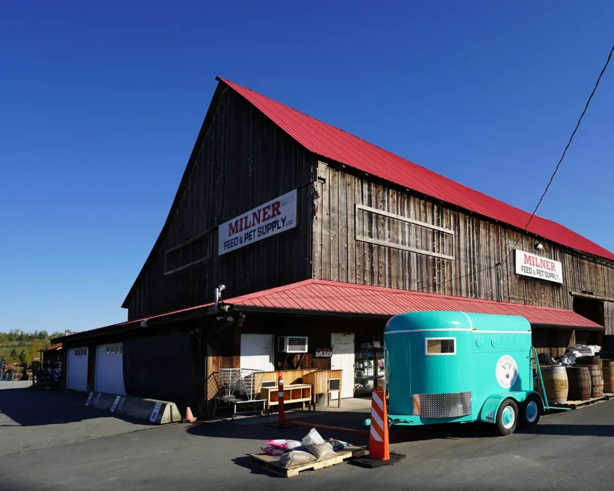 The Milner Feed & Pet Supply barn: a tall weathered timber building with a red roof and Milner signs, a teal horse trailer parked out front