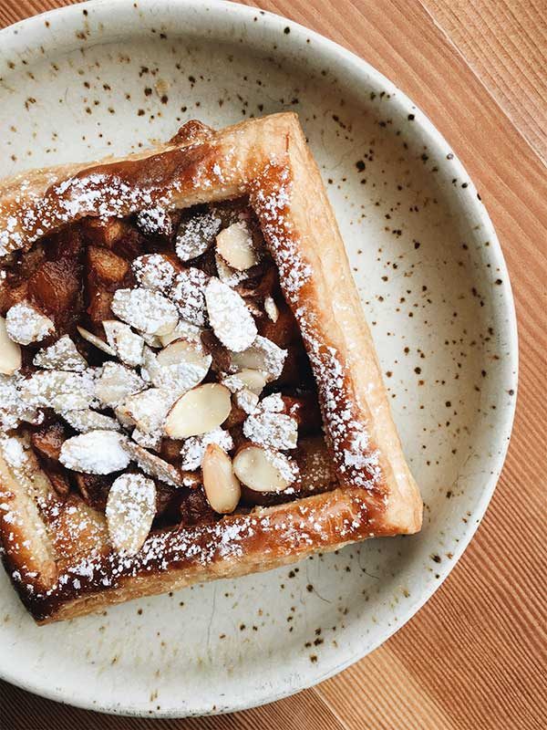 A square fruit pastry topped with flaked almonds and icing sugar on a speckled plate, from Oldhand's bakery