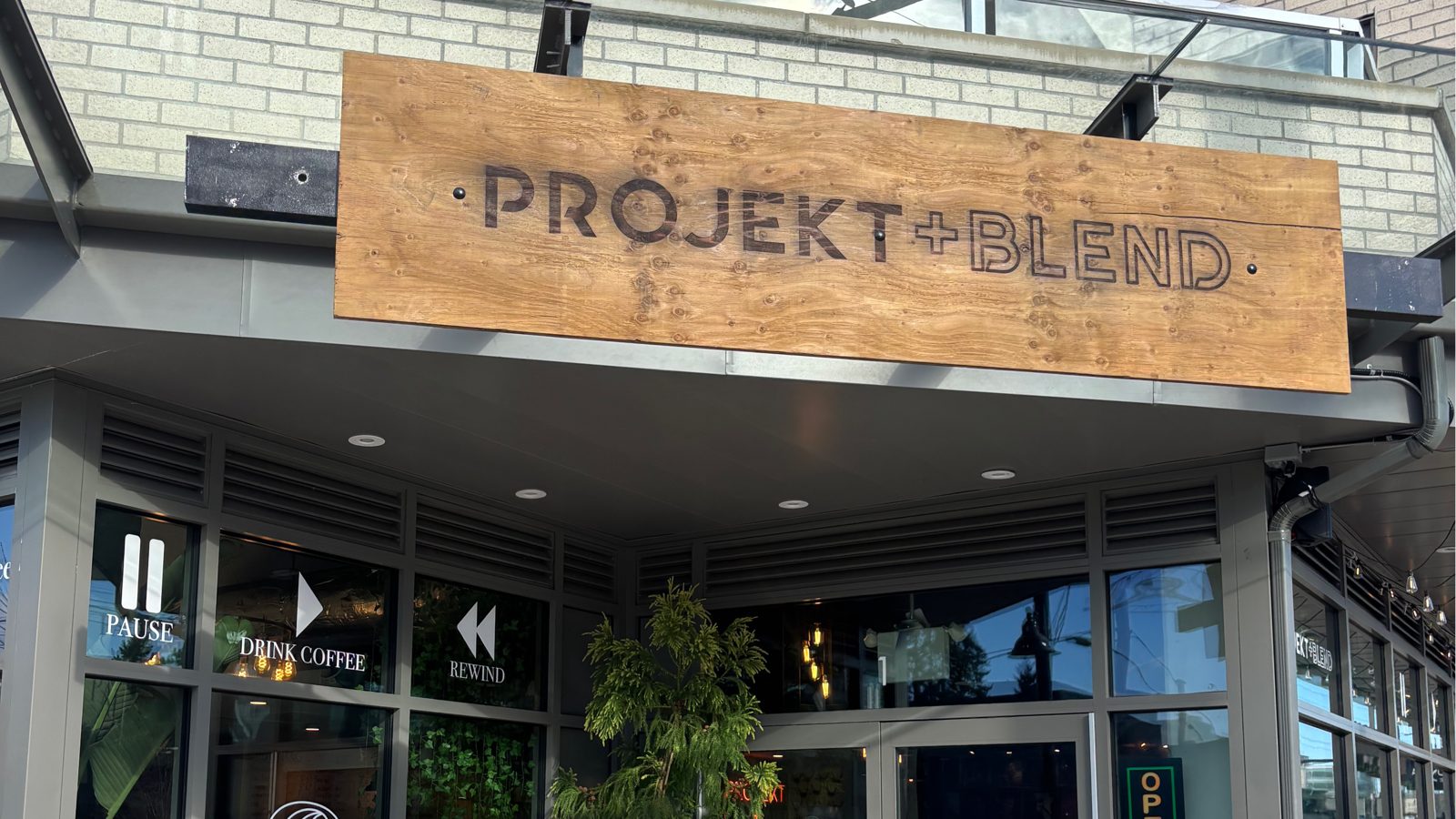 The wooden Projekt+Blend sign above the café's glass front on Fraser Highway, with window decals reading Pause, Drink Coffee and Rewind