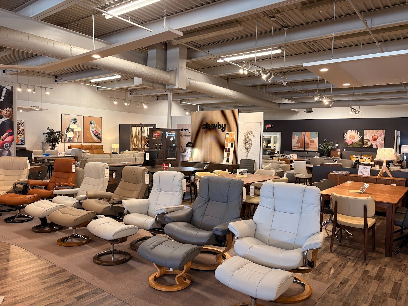 A row of leather Stressless-style recliners with matching ottomans on the ScanDesigns Langley showroom floor, with dining sets behind