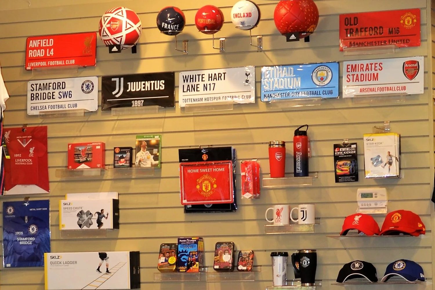 A Soccerwest wall of club merchandise with Premier League street signs, balls, mugs and caps