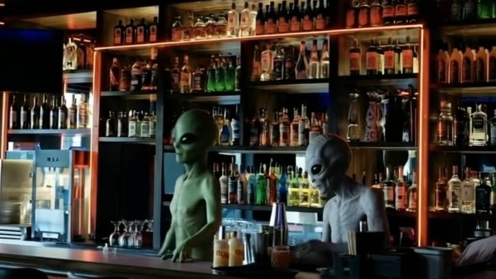 The back bar at Steven's, with lit shelves of bottles and two rubbery alien figures, part of the October alien-takeover decor, standing behind the counter