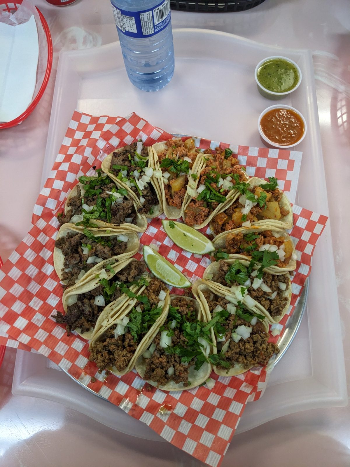 A tray of a dozen street tacos at Tacoholic on doubled corn tortillas, with lime and two salsas