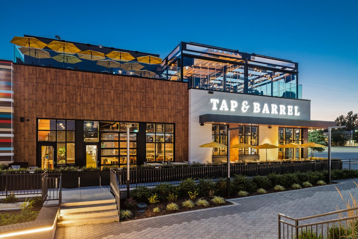 Tap & Barrel Willowbrook at dusk, with its glassed-in rooftop patio and yellow umbrellas above the street-level entrance
