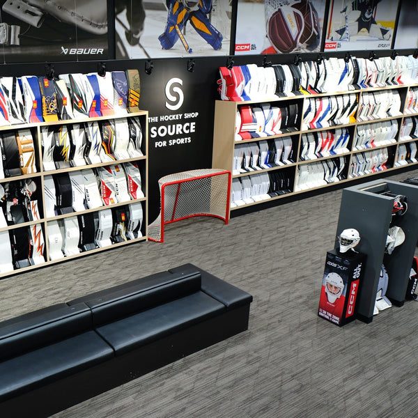 The goalie department at The Hockey Shop: a wall of goalie pads and blockers, a hockey net and a bench for trying gear on