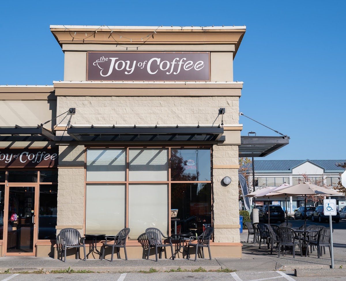 The Joy of Coffee's storefront in Murrayville Square: a tall sign over the corner, big windows and patio tables and chairs out front