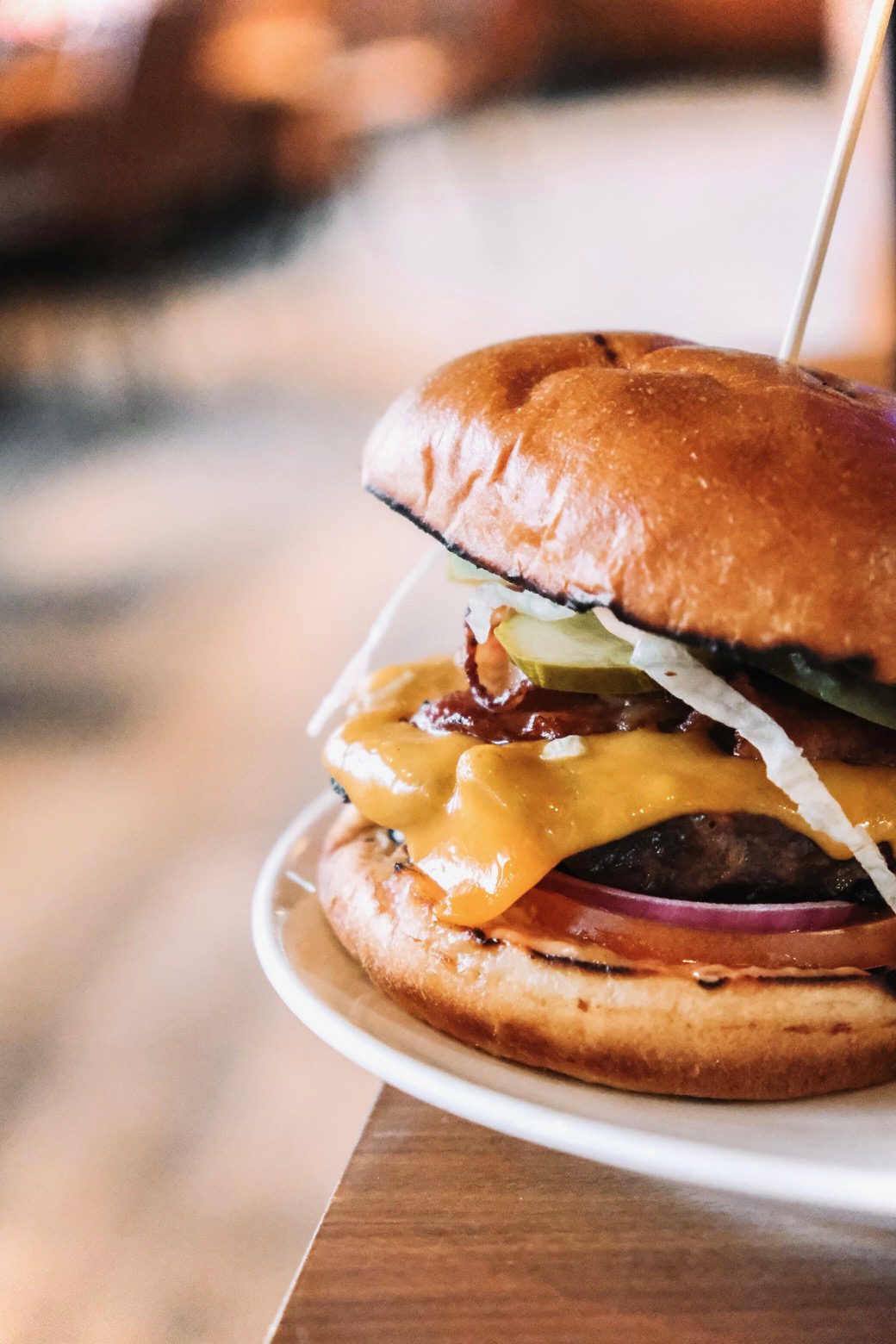 Close-up of The Lodge's bacon cheddar burger on a toasted bun with pickles, onion and tomato