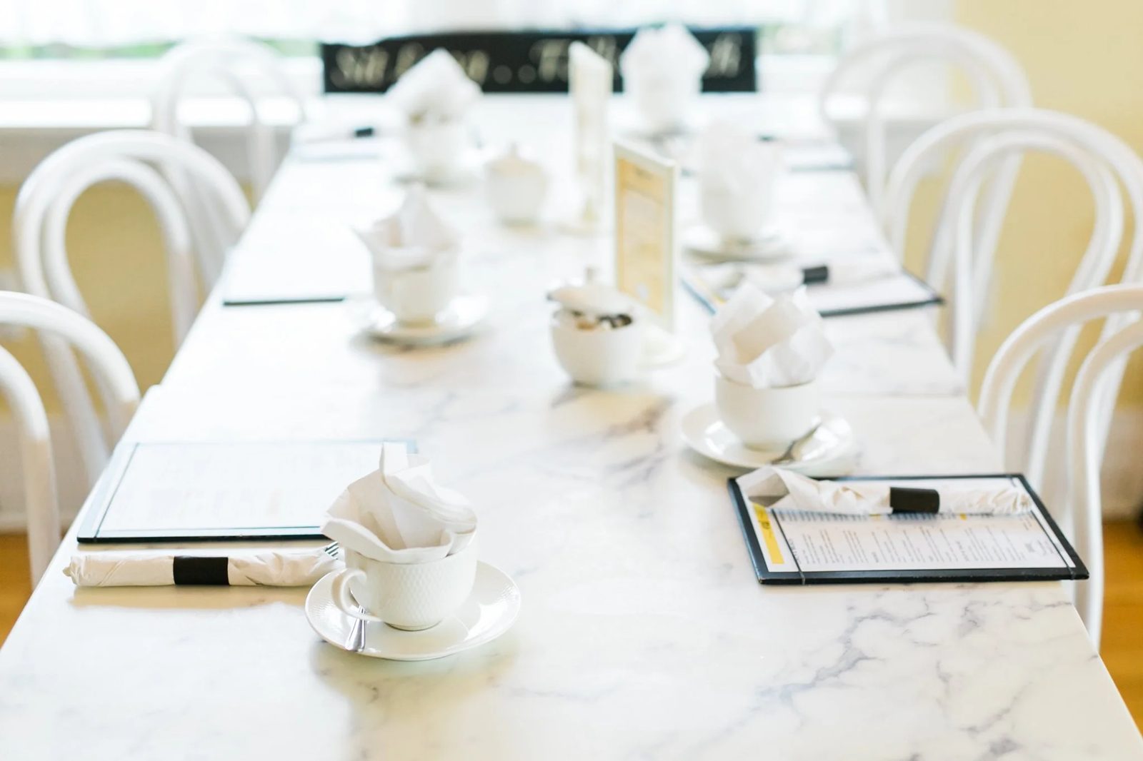 A long marble table set for high tea with white teacups and menus inside Tracycakes' Murrayville café