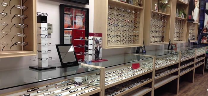 Frame displays inside Vision Care Centre: wooden wall racks of glasses and glass-topped counters lined with eyeglass frames