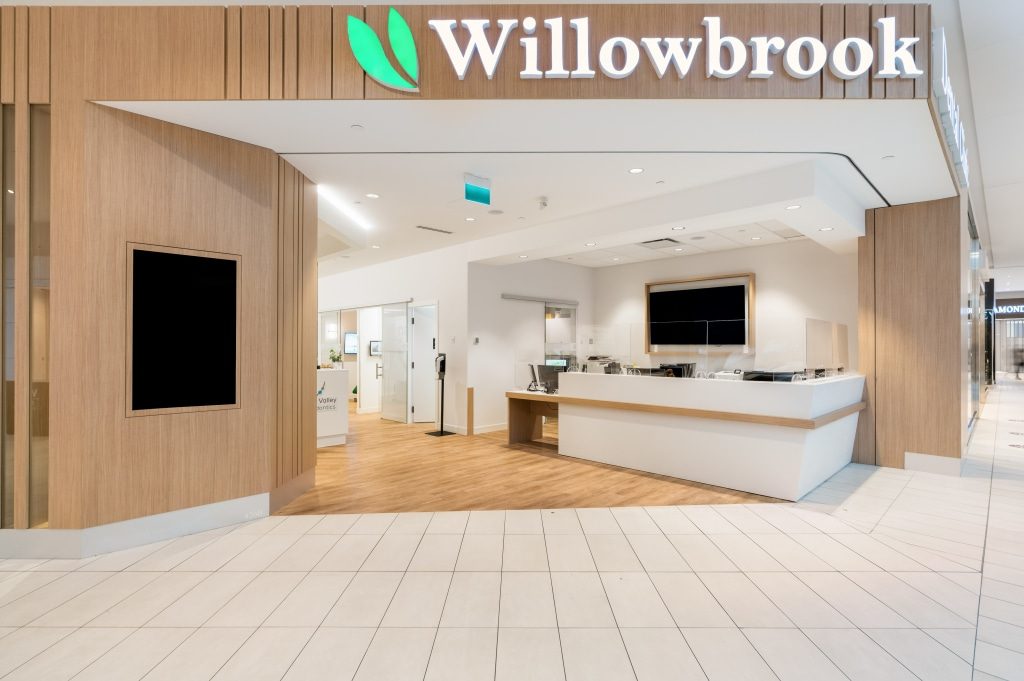 The Willowbrook Dental Clinic entrance inside Willowbrook Shopping Centre: wood-slat walls, a lit Willowbrook sign overhead and a white reception counter beyond the open front
