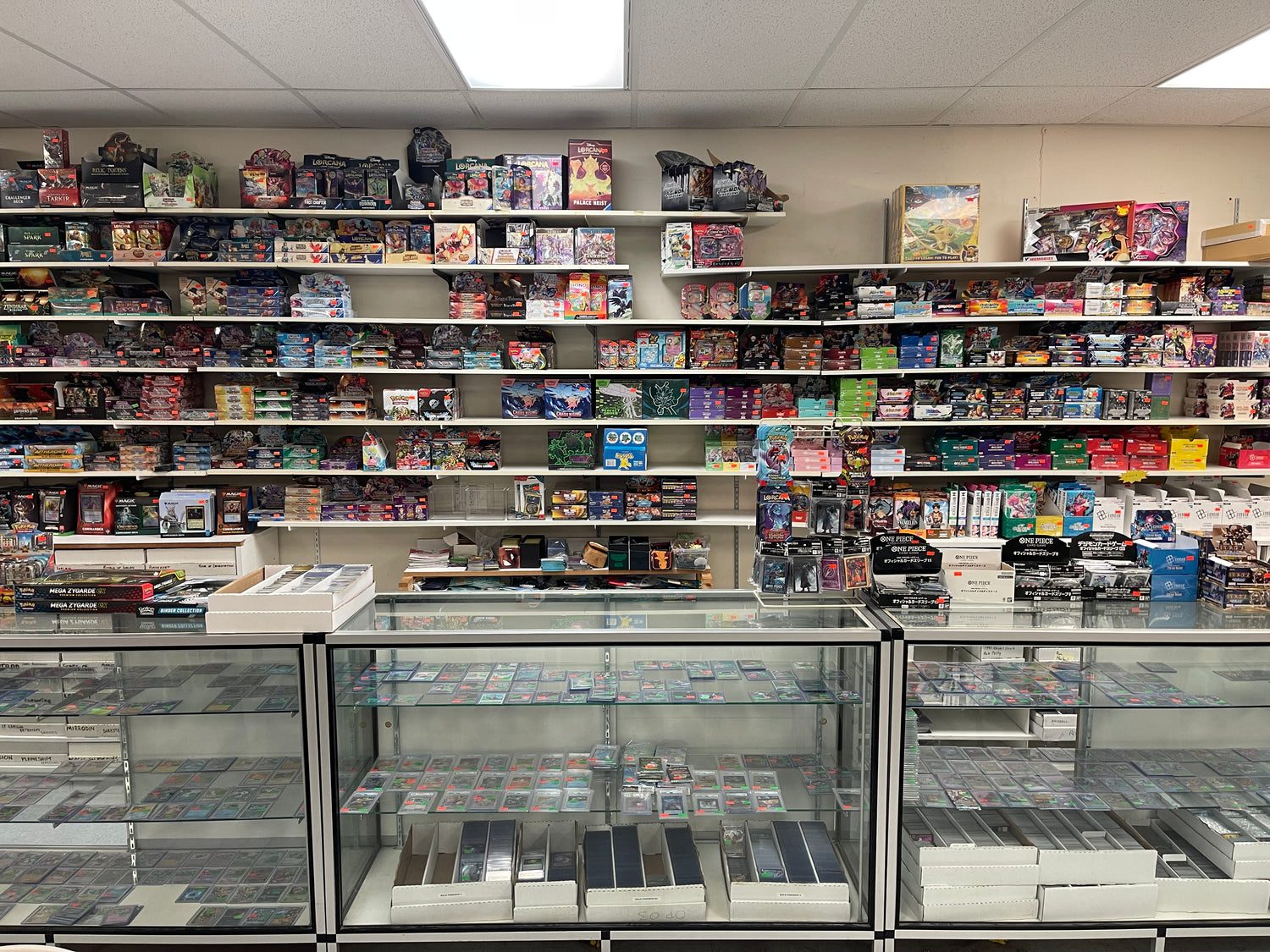 Glass cases of single trading cards at Wiser's Collectibles, with shelves of boxed card games and collectibles behind
