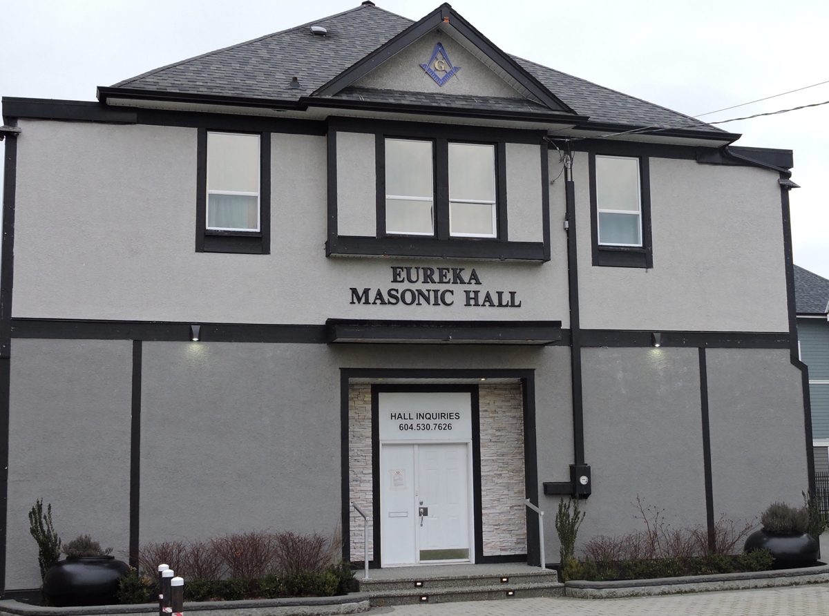 The front of Eureka Masonic Hall on Fraser Highway, a two-storey grey building with black trim and the square and compass in the gable