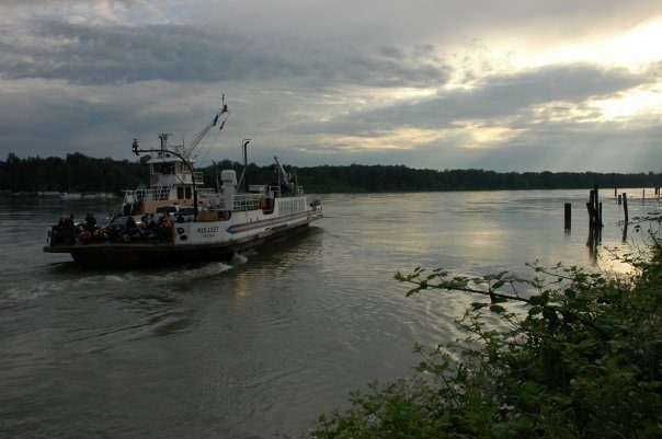 A small car ferry crossing the Fraser River under a cloudy sky