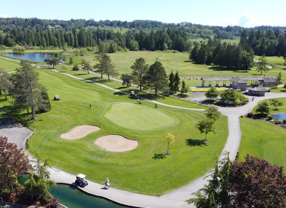 Aerial view of Hazelmere Golf Course in summer: a green with two bunkers, cart paths, a pond and the covered range behind