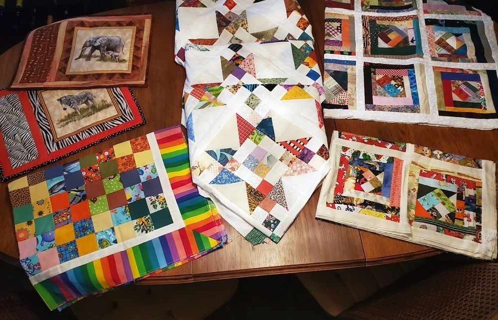 Finished community quilts and placemats laid out on a wooden table