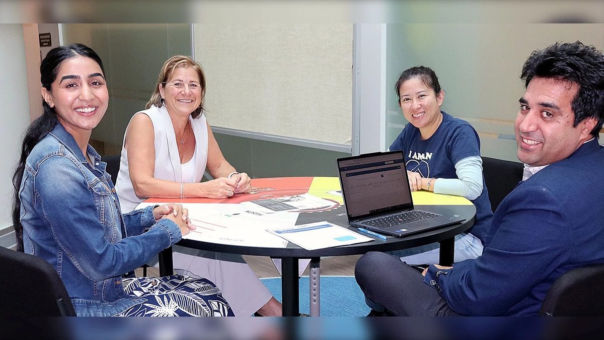 Four smiling people around a table with papers and a laptop, from the school district's story on its newcomer welcome team